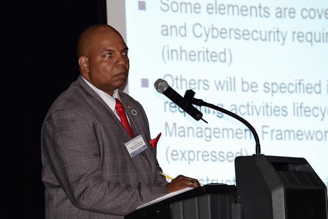 Man speaks into microphone at podium with screen behind him.