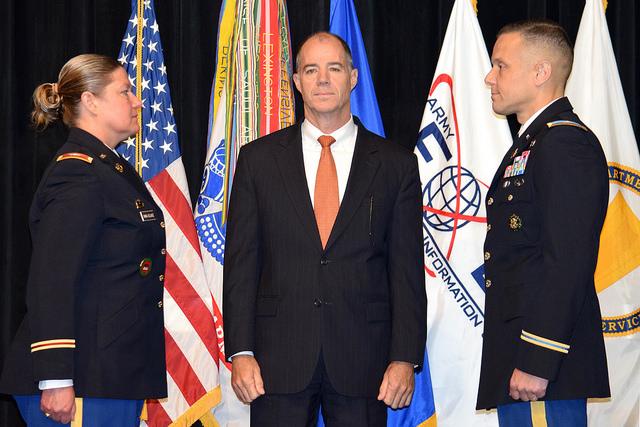 Three people stand on stage in front of flags.