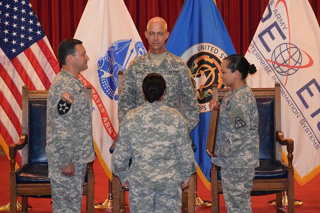 Four soldiers stand on stage in front of flags.